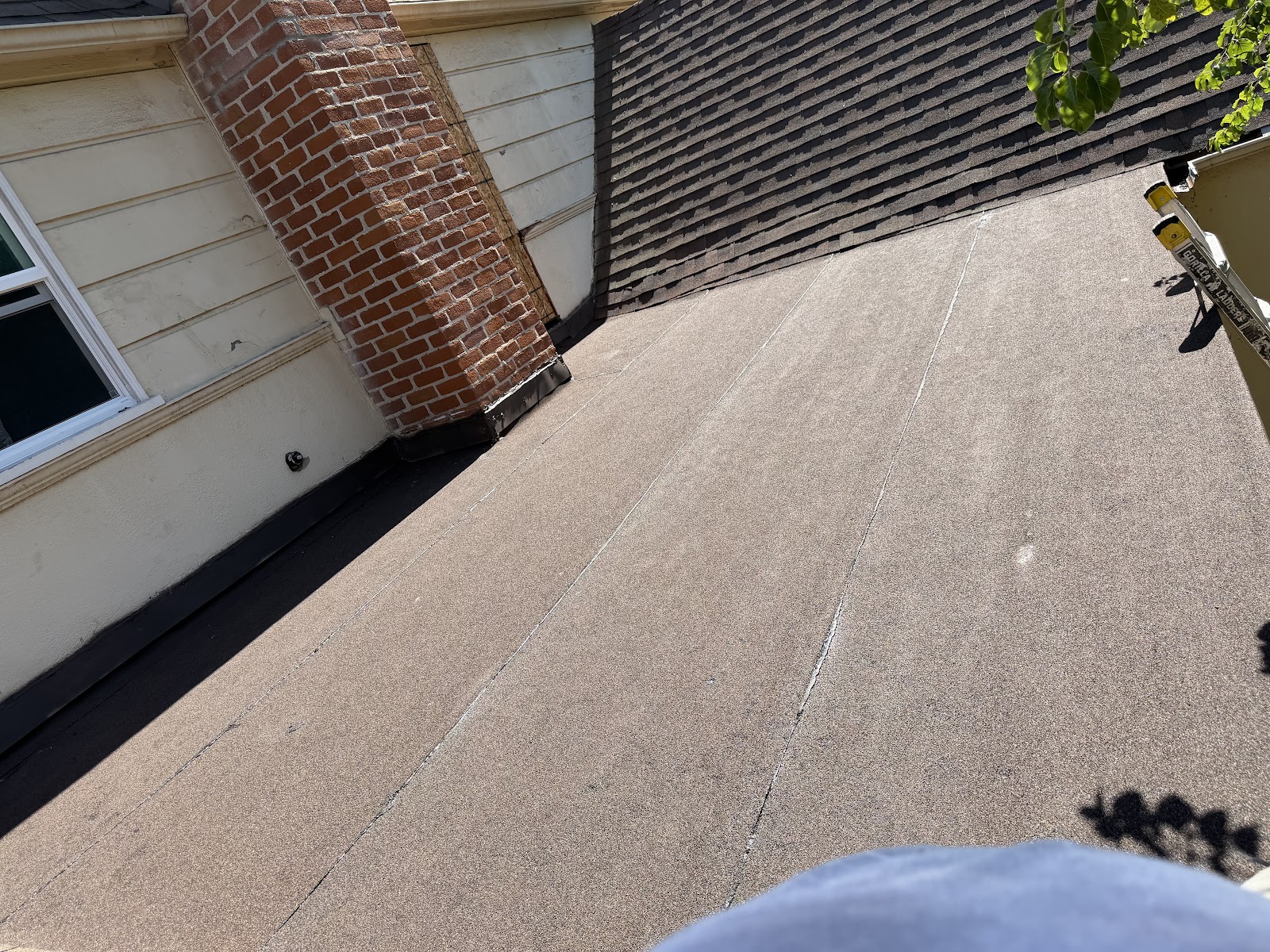 Finished low-slope roofing membrane beside a shingle roof and brick chimney